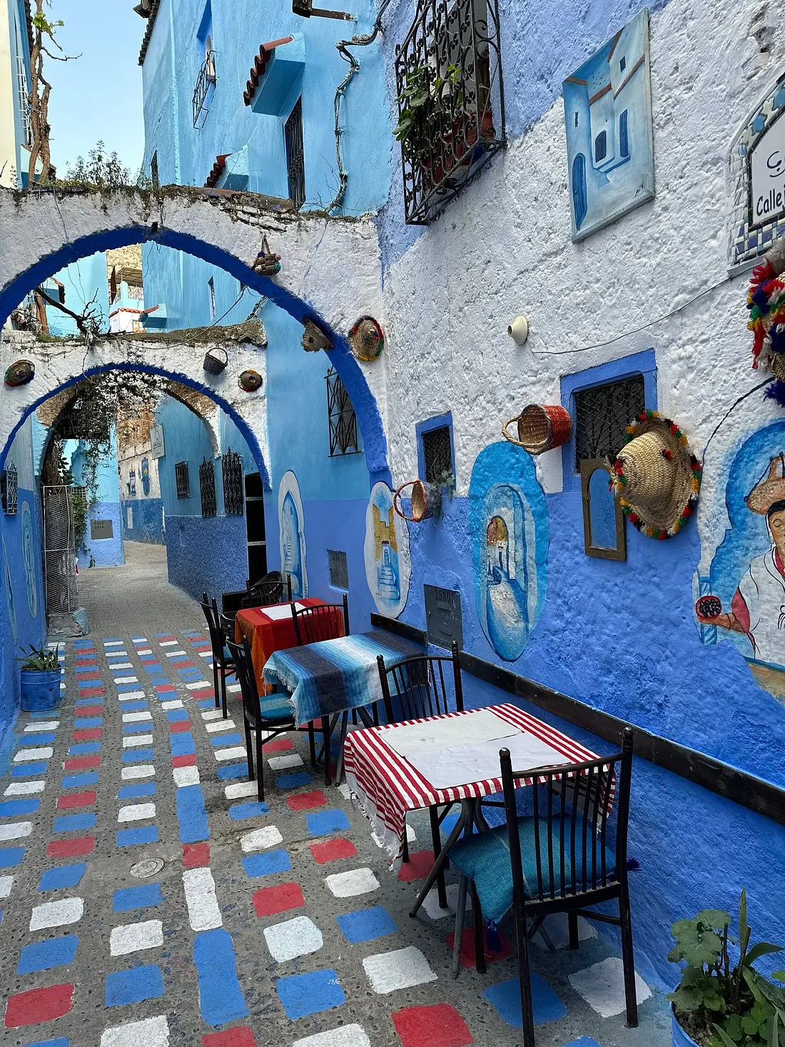 A café terrace on a blue-painted street in Chefchaouen, tables in the morning shade