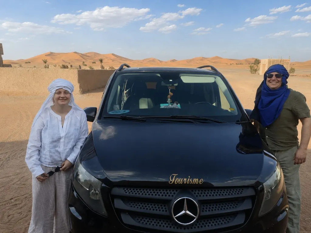 Travellers standing beside a tour van on the desert road approaching Merzouga