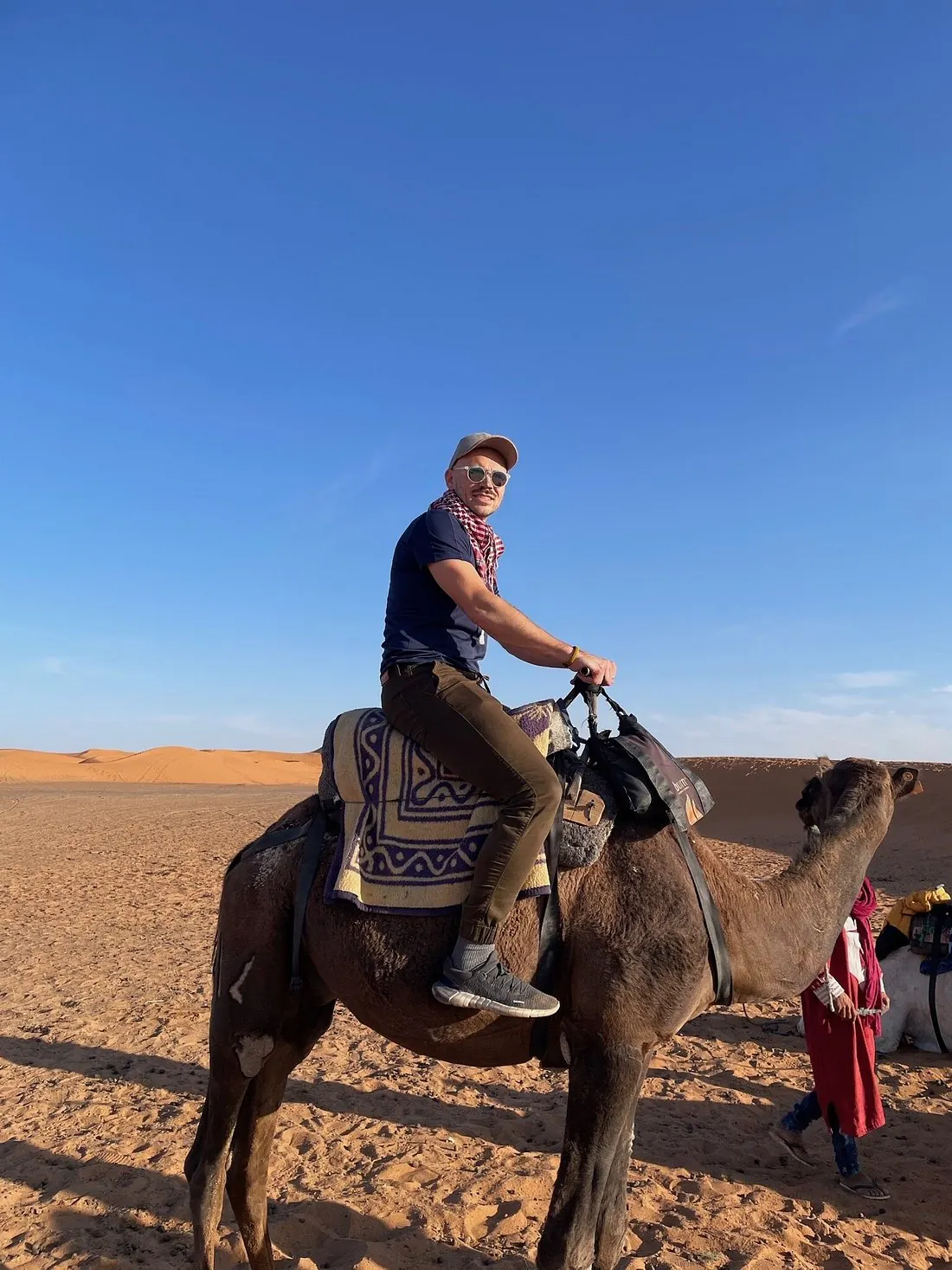 A traveller riding a camel under a clear blue Moroccan sky, relaxed and unhurried