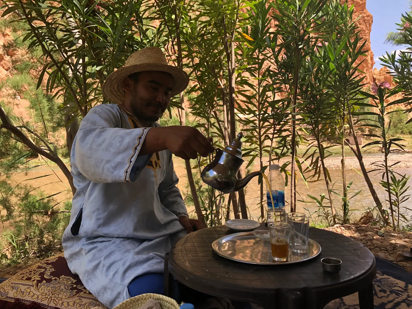 Berber guide pouring traditional mint tea at a riverside rest stop in the Atlas