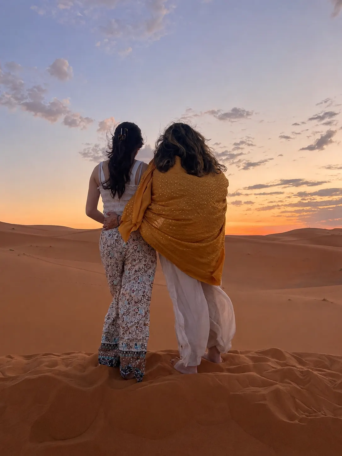 Two travellers silhouetted against an amber Sahara sunset