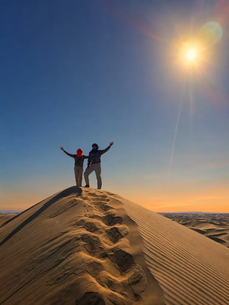 Travellers celebrating at the summit of a sand dune at sunrise
