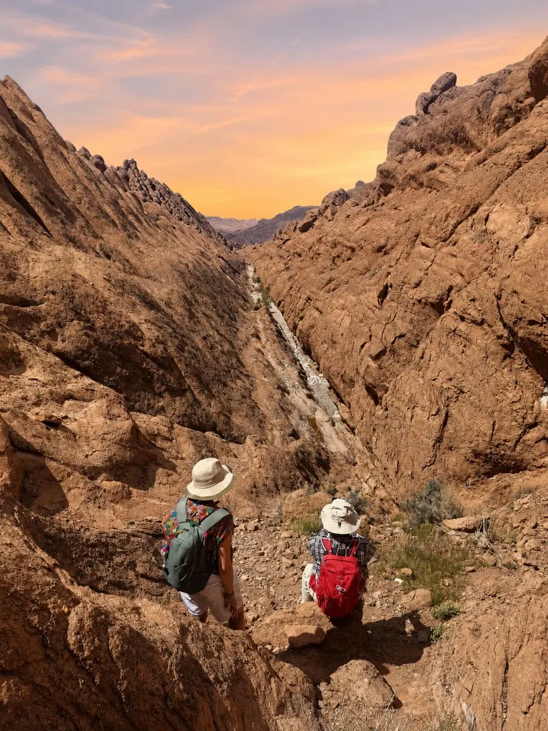 Two trekkers overlooking a deep canyon at sunset in the Todra Gorge