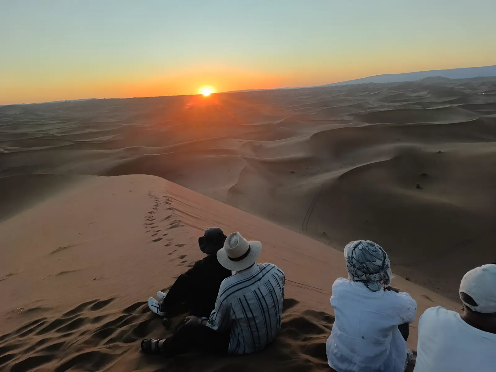 Travellers watching the Sahara sunrise from the dune crest