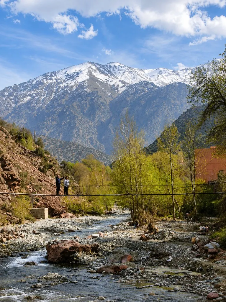 A suspension bridge over the Ourika river with snow-capped Atlas Mountains behind